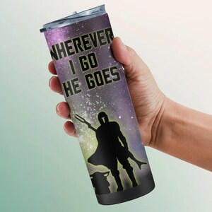 Puede incluir: Un vaso de acero inoxidable negro con un estampado de galaxia y el texto "WHEREVER I GO HE GOES". Una silueta de un Mandaloriano y Grogu se encuentra en el centro del vaso.