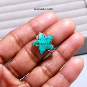 Könnte beinhalten: Ein türkisfarbener Sternring mit einem silbernen Band. Der Ring hat einen hellblau-grünen Stein mit dunkelblauen Adern. Der Ring ist ein einzigartiges Schmuckstück. Der Text "JewelsByShreyaUS" ist sichtbar.