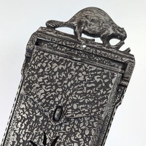 May include: A vintage cast iron mailbox featuring a beaver design on top. The mailbox has a textured surface and a star-shaped opening. It is painted in a silver colour and has a hook for hanging.