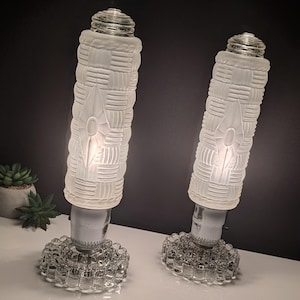 May include: A white ceramic mug with a black handle and the text "But First, Coffee" in a black, handwritten-style font. The mug is on a white surface.