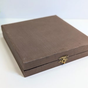 May include: A brown rectangular box with a gold latch. The box has a textured surface and is closed.