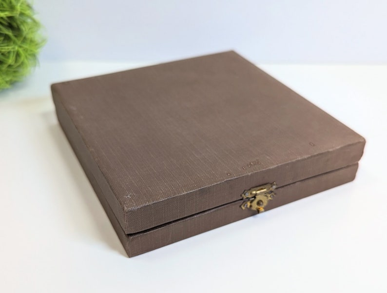 May include: A brown rectangular box with a gold latch. The box has a textured surface and is closed.