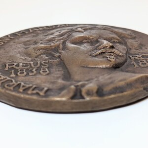 May include: A bronze medal with a portrait of a man with a beard and mustache. The medal is inscribed with the text "MARIANO FORTUNY MARSAL REUS 1838 ROMA 1874".