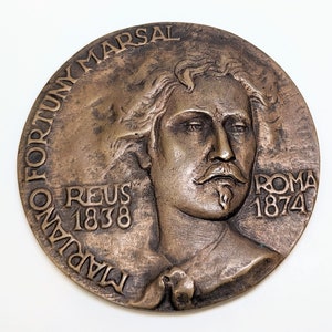 May include: A bronze medal with a portrait of a man with a beard and the text "TADIANO FORTUNY MARSAL REUS 1838 ROMA 1874".