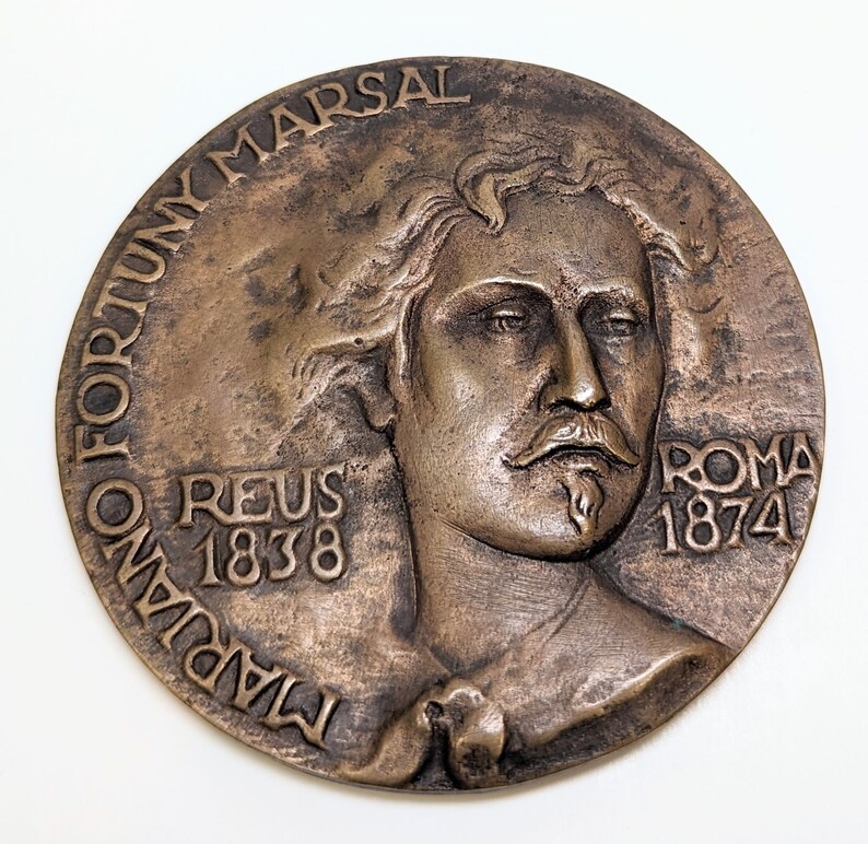 May include: A bronze medal with a portrait of a man with a beard and the text "TADIANO FORTUNY MARSAL REUS 1838 ROMA 1874".