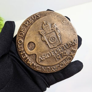 May include: A bronze medal with the inscription "Anno Fortunuy 1974" and the words "Olent De Reus" around the edge. The medal features a coat of arms with a crown and a wreath.