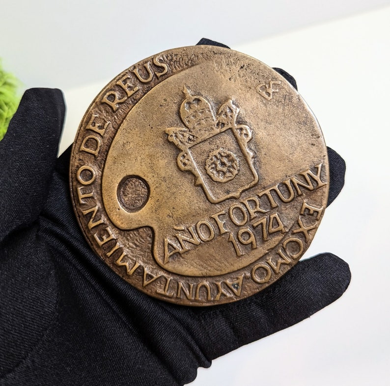 May include: A bronze medal with the inscription "Anno Fortunuy 1974" and the words "Olent De Reus" around the edge. The medal features a coat of arms with a crown and a wreath.