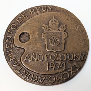 May include: A bronze medal with a papal coat of arms and the text "A&ntilde;o Fortuny 1974" and "Movimiento de Reus" around the edge.