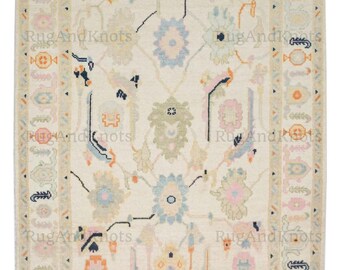 May include: Cream-colored area rug with a central floral design in pastel shades of blue, pink, and green. The rug features a detailed border with repeating geometric and floral patterns. The text "RugAndKnots" is visible.