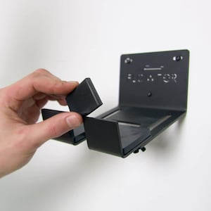 May include: A black metal wall mount with the text "FLOAT-FOR" printed on it. The mount has two rubber pads that can be used to hold a device.