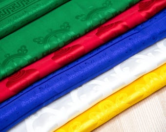 May include: Five fabric squares stacked on top of each other. The squares are green, red, blue, white, and yellow. The fabric has a repeating pattern of a wheel with spokes and a circle in the center. The fabric is folded in half and the edges are visible.