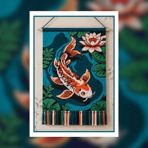 Könnte beinhalten: Ein rechteckiger Wandbehang mit einem gehäkelten Koi-Karpfen in Orange, Weiß und Schwarz, der in tiefblauem Wasser schwimmt. Das Design zeigt grüne Seerosenblätter und eine weiße Lotusblüte. Das Stück hängt an einem Holzstab mit bunten Quasten.