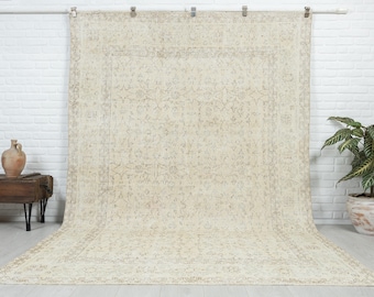 May include: A large, off-white vintage rug with a floral pattern. The rug has a worn, distressed look and is hanging on a white wall.