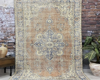 May include: A vintage rug with a faded, distressed look. The rug has a central medallion with a floral design in shades of blue and cream, surrounded by a border with a repeating pattern. The rug is beige, cream, and blue.