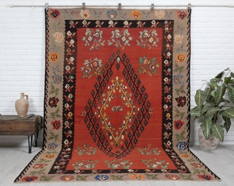 May include: A traditional red, black, and beige rug with a diamond pattern in the center and floral motifs along the border.