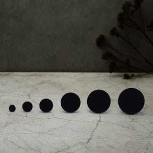 May include: A set of seven black round stickers of varying sizes, arranged in order from smallest to largest on a light gray surface.