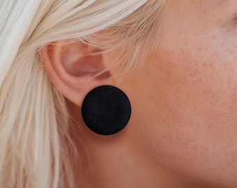May include: A pair of black round stud earrings. The earrings are made of a smooth, matte material.