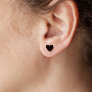 Op de afbeelding: Een close-up van een oor met een kleine zwarte hartvormige oorbel.