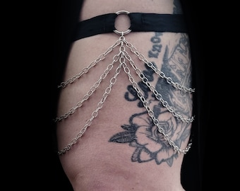 May include: A black garter with a silver ring and multiple silver chains hanging down.