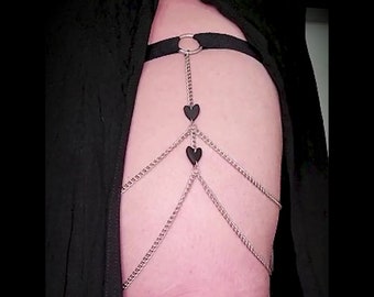 May include: A silver chain with three black heart charms attached. The chain is connected to a black elastic band with a silver ring.