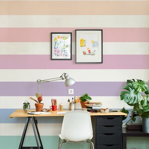 K&ouml;nnte beinhalten: Ein heller Holzschreibtisch mit einem schwarzen Metallgestell und einem wei&szlig;en Stuhl. Der Schreibtisch hat einen schwarzen Schubladenblock und eine Topfpflanze. Die Wand hinter dem Schreibtisch ist mit horizontalen Streifen in Pastellfarben gestrichen. An der Wand h&auml;ngen auch zwei gerahmte Bilder, eines mit einem bunten Alphabet und das andere mit einer einfachen Illustration.