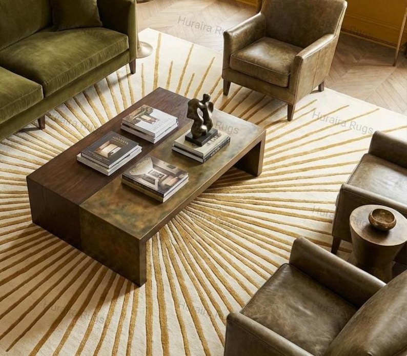 May include: An overhead shot of a living room with a large, rectangular coffee table made of wood and metal. The table is adorned with books and a sculpture. The room features a patterned rug, a green sofa, and leather armchairs.
