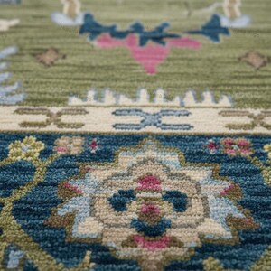 May include: Close-up of a detailed rug with a traditional design. The rug features a combination of colors, including green, blue, pink, and cream. The pattern includes floral and geometric elements, creating a textured surface.