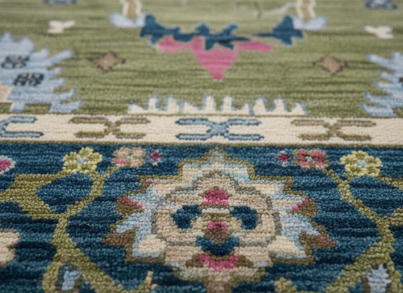 May include: Close-up of a detailed rug with a traditional design. The rug features a combination of colors, including green, blue, pink, and cream. The pattern includes floral and geometric elements, creating a textured surface.