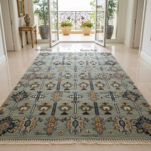 Könnte beinhalten: Ein rechteckiger, hellblauer Teppich mit einem komplizierten geometrischen Muster. Das Design enthält marineblaue, braune und goldfarbene Akzente. Der Teppich hat einen Fransen an den Enden und liegt auf einem polierten Boden. Maße in Zentimetern.