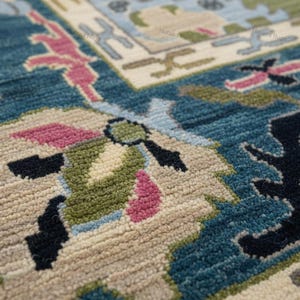 May include: Close-up of a teal rug with a detailed floral pattern. The rug features a combination of colors, including teal, beige, pink, green, and black. The design is intricate and appears to be hand-knotted, showcasing a traditional style.