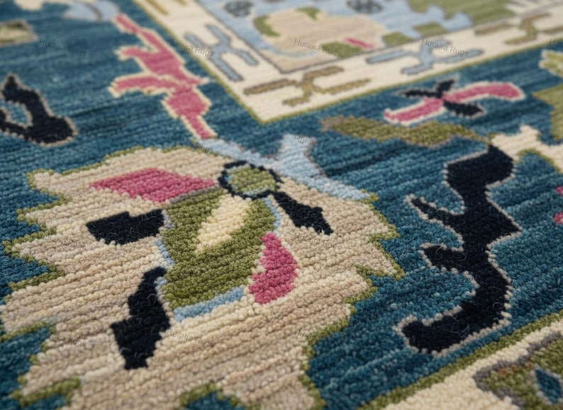 May include: Close-up of a teal rug with a detailed floral pattern. The rug features a combination of colors, including teal, beige, pink, green, and black. The design is intricate and appears to be hand-knotted, showcasing a traditional style.