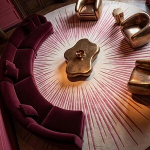 Curved magenta sofa surrounds 8x8 round sunburst rug, warm pink to burgundy rays, modern statement