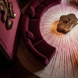 Corner overhead view, 8x8 round sunburst rug beside curved sofa, glowing cream center to deep burgundy edge