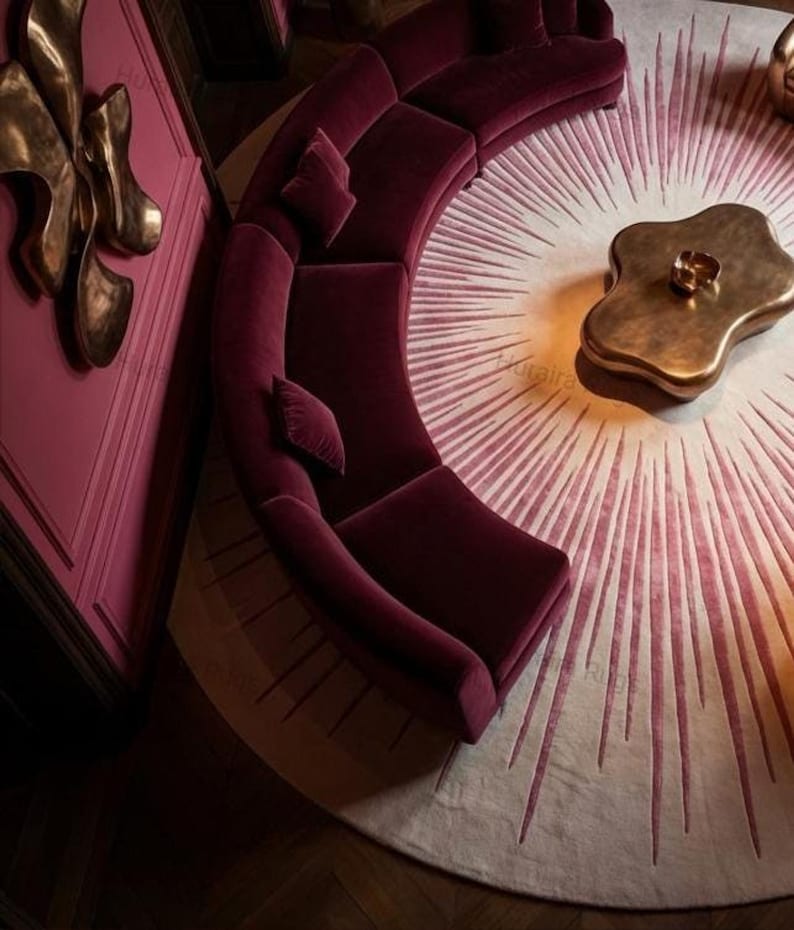 Corner overhead view, 8x8 round sunburst rug beside curved sofa, glowing cream center to deep burgundy edge