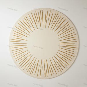 May include: A circular rug in cream with a sunburst pattern. The rug has a central cream circle, encircled by radiating golden-brown lines. The lines are evenly spaced, creating a striking pattern. The rug is likely made of a soft material, with a diameter of approximately 150 cm.