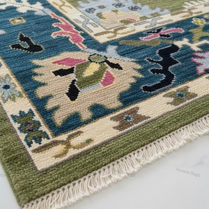 May include: Close-up of a rectangular rug with a detailed pattern. The rug features a teal, beige, and green color scheme with floral and geometric designs. The border is green, and the rug has a fringe.