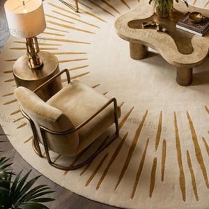May include: Overhead view of a living room with a cream rug featuring gold sunburst designs. The room includes a beige armchair with a metal frame, a unique coffee table, and a brass lamp. The rug has a diameter of approximately 200 cm.