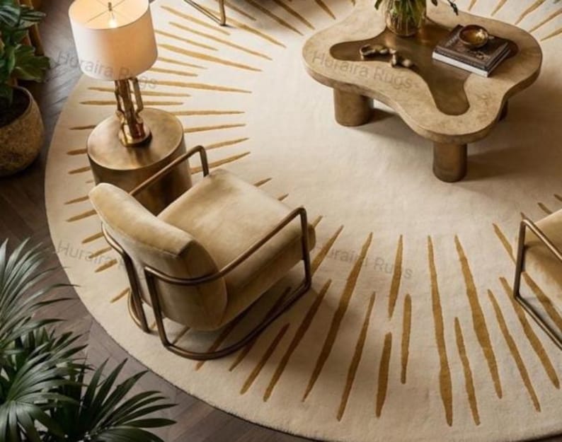 May include: Overhead view of a living room with a cream rug featuring gold sunburst designs. The room includes a beige armchair with a metal frame, a unique coffee table, and a brass lamp. The rug has a diameter of approximately 200 cm.