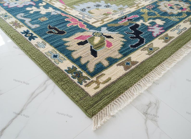 May include: A corner view of a detailed area rug with a traditional design. The rug features a teal, green, and cream color palette with floral and geometric patterns. The edges are finished with a green border and fringe.