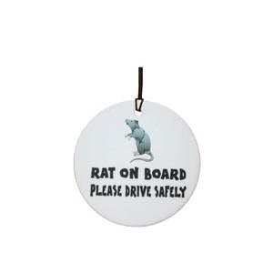 May include: White round ceramic car air freshener with a black string for hanging. It features a cartoon image of a gray rat and the text "Rat on Board Please Drive Safely".