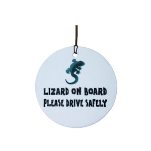 Puede incluir: Ambientador de coche redondo de cerámica blanca con un gráfico de lagarto negro y el texto "Lizard on board please drive safely".