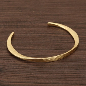 Puede incluir: Un brazalete de oro martillado. El brazalete está hecho de una sola pieza de metal que se dobla en un círculo.