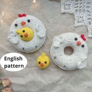 May include: Three crocheted amigurumi toys: a white chick with a yellow chick inside, a white chick shaped like a donut, and a small yellow chick. The toys are on a beige fabric background.
