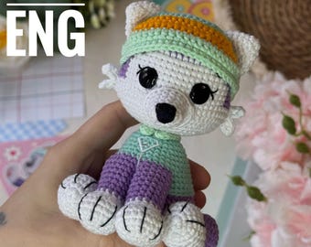 Può includere: Orsetto polare all'uncinetto fatto a mano, bianco con occhi e naso neri. Indossa un completo e un cappello verde menta e viola. Il testo "PATTERN ENG" è in alto a sinistra.