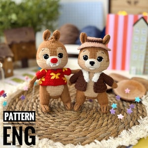 May include: Two handmade crochet chipmunk dolls. One chipmunk wears a red sweater with yellow floral accents, the other wears a brown jacket and hat. The dolls are on a woven mat with the text "PATTERN ENG".
