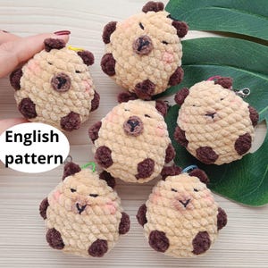 May include: Six crocheted plush toys shaped like sheep with brown accents. The sheep are beige and have black eyes and a black nose. The toys are all about 3 inches tall and have a loop for hanging. English pattern.