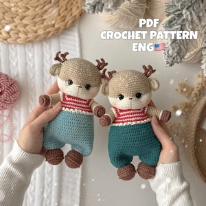 Può includere: Due bambole di cervo all'uncinetto, ciascuna con testa beige, corna marroni e mani e piedi marroni. Indossano camicie a righe rosse e bianche e pantaloni blu. Il testo "PDF CROCHET PATTERN ENG" è visibile.
