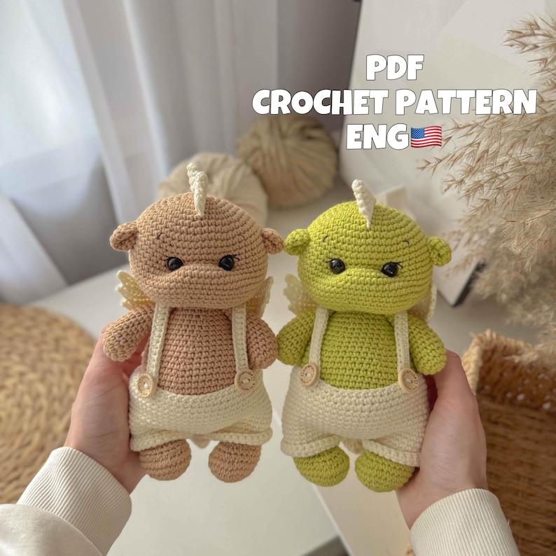 May include: Two crocheted amigurumi toys, one brown and one green, with white wings and overalls. The toys have button eyes and are holding a small white flower.