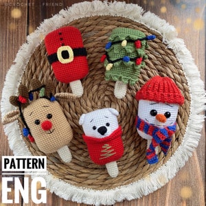 Op de afbeelding: Vijf gehaakte kerst-ijsjes: een sneeuwpop, een rendier, een kerstboom, een ijsbeer en de kerstman. Elk ornament is gemaakt van garen in verschillende kleuren en heeft een stokachtige basis.