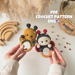 May include: Two handmade crochet baby rattles, one yellow and black bee and one black and red ladybug, each with a wooden ring. The rattles are held in hands. The text "PDF CROCHET PATTERN ENG" is visible in the image.